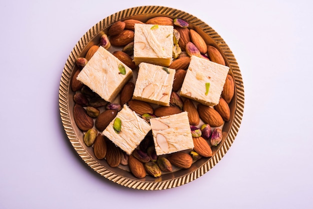 Patisa lub Soan Papdi to popularny indyjski płatkowy i chrupiący deser w kształcie kostki. Podawany z migdałami i pistacjami w talerzu na nastrojowym tle. Selektywne skupienie