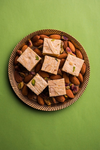 Patisa lub Soan Papdi to popularny indyjski płatkowy i chrupiący deser w kształcie kostki. Podawany z migdałami i pistacjami w talerzu na nastrojowym tle. Selektywne skupienie