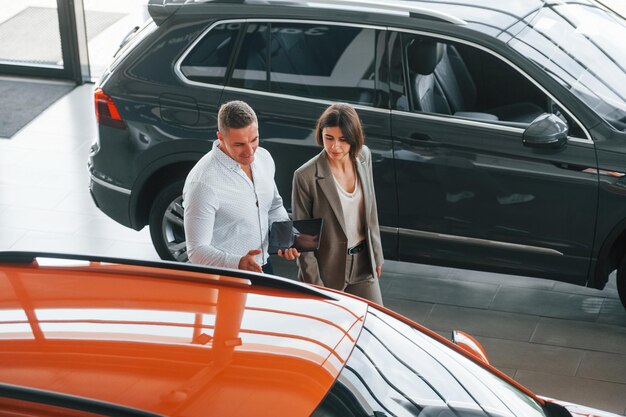 Patrząc na samochód Mężczyzna w stroju wizytowym pomaga klientowi w wyborze samochodu