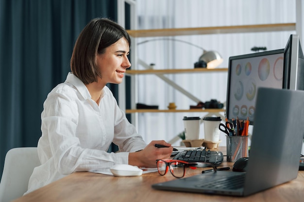 Patrząc na wyświetlacz Kobieta projektantka pracująca w biurze za pomocą komputera