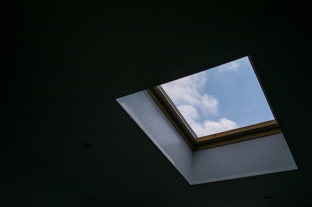 Patrząc w błękitne pochmurne niebo przez nowoczesne kwadratowe okno sufitowe