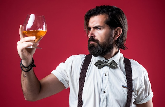 Patrząc wielki elegancki mężczyzna barman przystojny hipster pijący rum szkło imprezowy goer z alkoholem brandy lub koniakiem brodaty mężczyzna w szelkach pić szkocką whisky brutalny facet barman nosić muszkę
