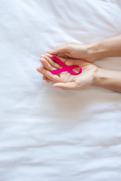 Październik Miesiąc świadomości Raka Piersi, Dorosły Kobieta Ręka Trzyma Różową Wstążkę Na Różowym Tle Do Wspierania Ludzi żyjących I Chorych. Koncepcja Międzynarodowego Dnia Raka Kobiet, Matki I świata