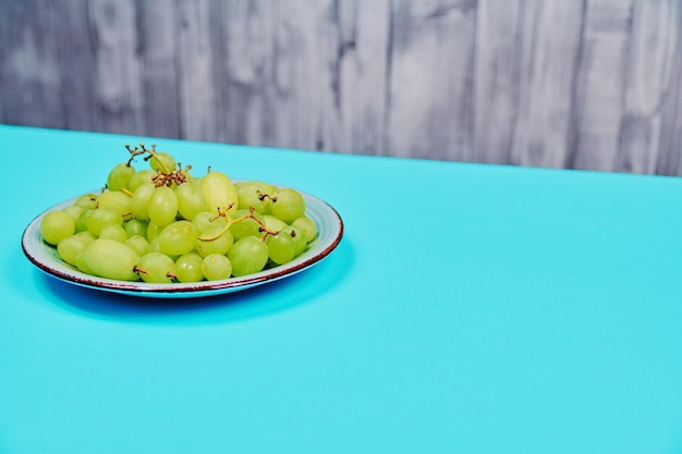 Pęczek apetycznych białych winogron stołowych na ukośnym niebieskim i szarym tle