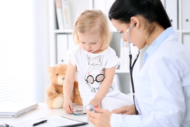 Pediatra opiekuje się dzieckiem w szpitalu. Mała dziewczynka jest badana przez lekarza stetoskopem. Koncepcja opieki zdrowotnej, ubezpieczenia i pomocy.