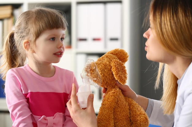 Pediatra pokazuje małej dziewczynce na zabawce, jak używać maski tlenowej