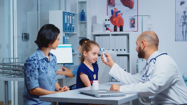 Pediatra sprawdzający temperaturę i pielęgniarka pisząca na komputerze. Lekarz specjalista medycyny udzielający świadczeń zdrowotnych konsultacje badanie diagnostyczne leczenie w gabinecie szpitalnym