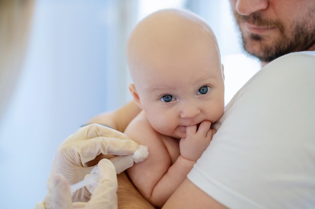 Pediatra w sterylnych rękawiczkach podaje noworodkowi zastrzyk domięśniowy za pomocą jednorazowej strzykawki