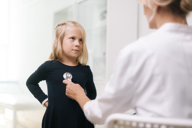 Pediatra ze stetoskopem badający młodą dziewczynkę o blond włosach