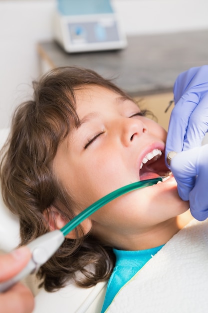 Pediatryczny dentysta egzamininuje troszkę chłopiec zęby w krzesło dentystów