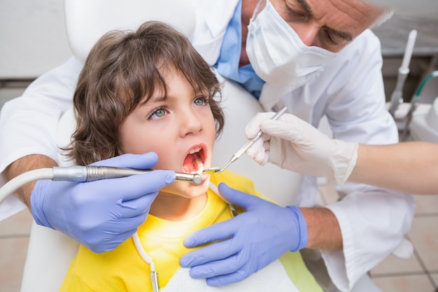 Pediatryczny dentysta egzamininuje troszkę chłopiec zęby w krzesło dentystów