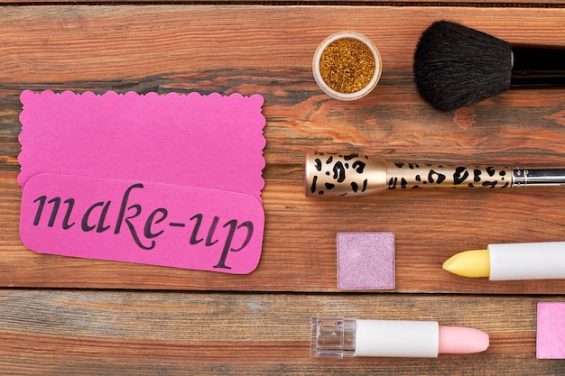 Pędzel i kosmetyki na drewnianym tle zestaw kosmetyków i różowa kartka z tekstem makijaż kobiecy k...