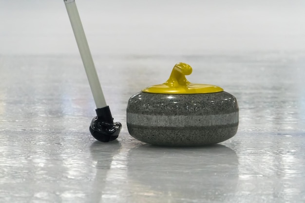 Pędzel i żółty Curling kamień na lodzie