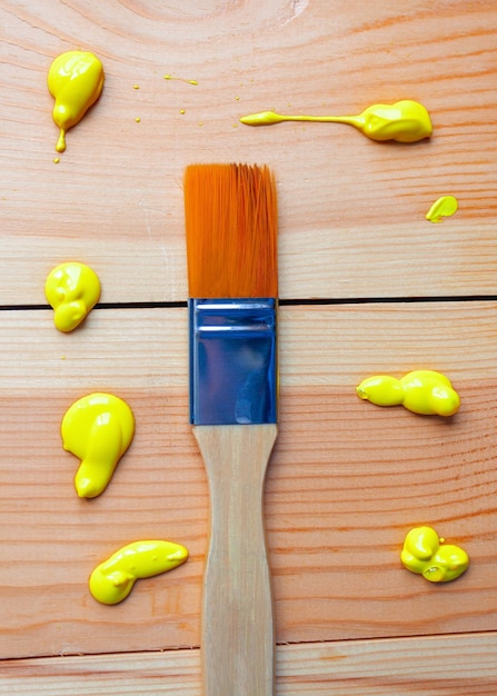 Pędzel z włosia syntetycznego leży na drewnianych deskach z kroplami żółtej farby akrylowej Naprawa DIY