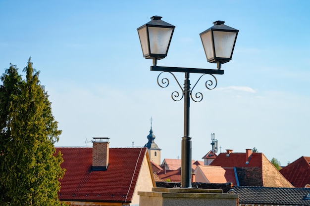 Pejzaż miejski z latarnią uliczną i dachami domów z kościołem Matki Boskiej Siedmiu Bolesnej w starym centrum w Slovenska Bistrica niedaleko Mariboru w Słowenii. Południowa Styria w Słowenii. Światło w słoweńskim mieście