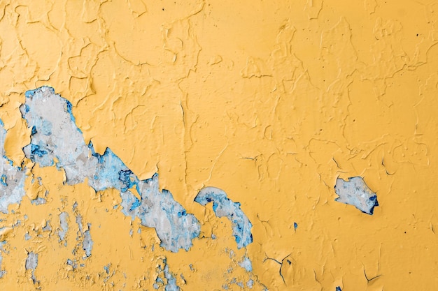Pęknięta żółta farba na niebieskiej betonowej ścianie