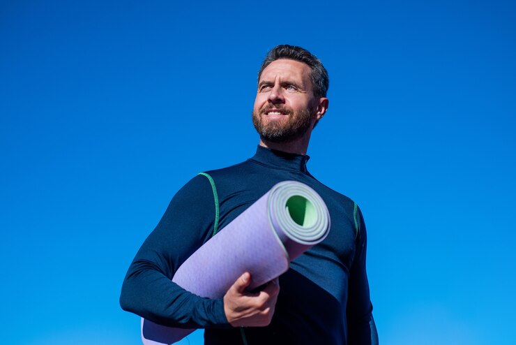 Zdjęcie pełen energii. moda męska fitness. sportowiec na tle nieba. przystojny sportowiec z matą do jogi. pewny siebie mężczyzna na stadionie. siłownia na świeżym powietrzu. muskularny facet trening sportowy. sukces sportowy.