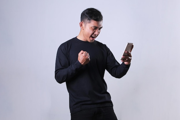 Pełen entuzjazmu i radości wyraz twarzy azjatyckiego mężczyzny patrzący na swojego smartfona