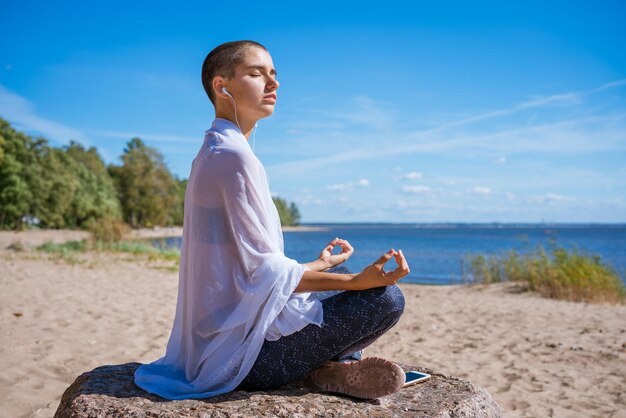 Pełen wdzięku kobieta robi asanę jogi na plaży w słuchawkach medytuje nad brzegiem morza