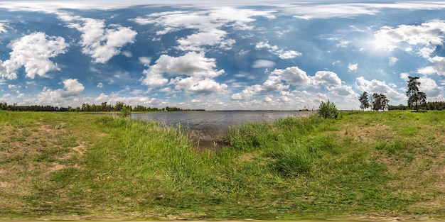 Pełna bezszwowa sferyczna panorama HDR 360 stopni kąta widzenia na trawiastym wybrzeżu ogromnego jeziora lub rzeki w słoneczny letni dzień i wietrzną pogodę z pięknymi chmurami w projekcji równokątnej Zawartość VR