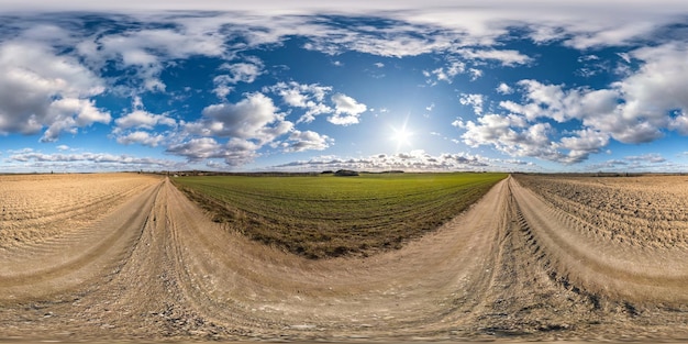 Pełna bezszwowa sferyczna panorama HDR 360 stopni kąta widzenia na żwirowej drodze wśród pól w wiosenny dzień z niesamowitymi chmurami w rzucie równoprostokątnym gotowa na zawartość wirtualnej rzeczywistości VR AR