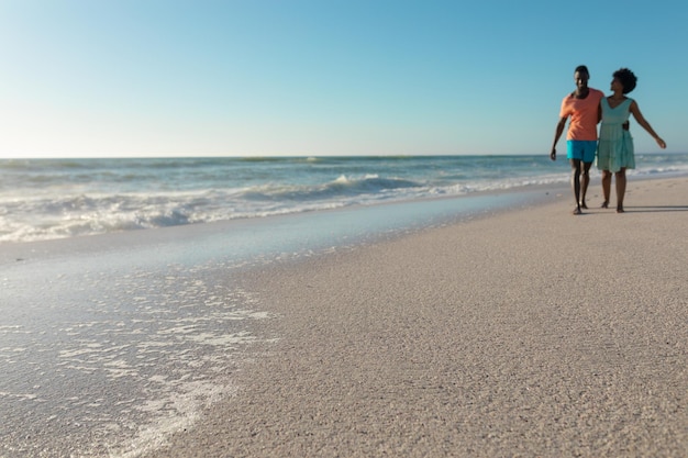 Pełna długość afrykańskiej amerykańskiej pary cieszącej się letnimi wakacjami podczas spaceru na plaży w słoneczny dzień