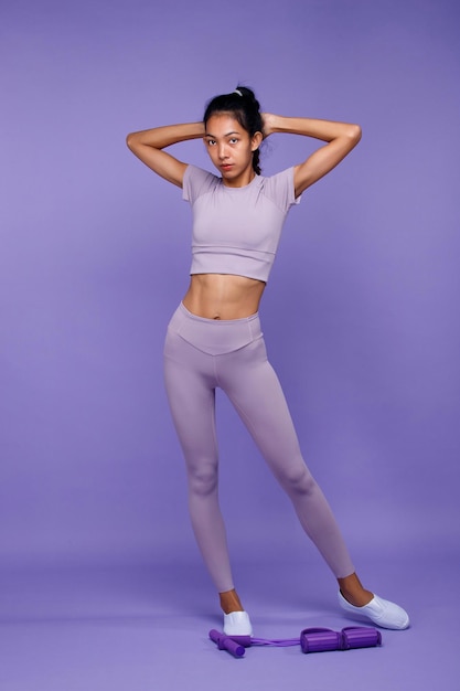 Pełna długość azjatyckiej szczupłej opalonej skóry Kobieta fitness stoi i pokazuje sześć paczek silnych mięśni brzucha z wyposażeniem w fioletowym tle koncepcji