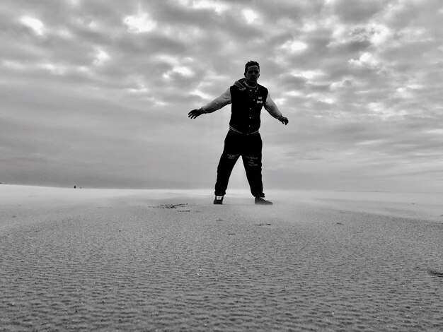 Zdjęcie pełna długość człowieka stojącego na piasku na chmurnym niebie na plaży