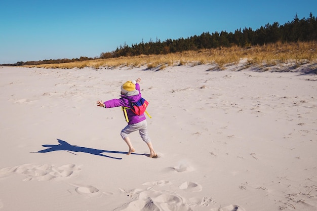 Zdjęcie pełna długość dziewczyny biegnącej po piasku na plaży na czyste niebo