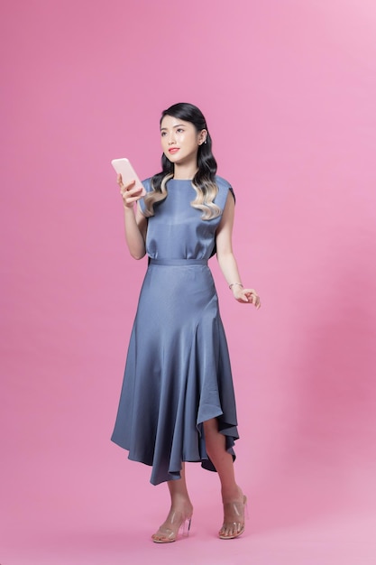 Pełna długość młoda azjatycka kobieta z telefonem komórkowym czatem online spacer idzie na białym tle na różowym tle