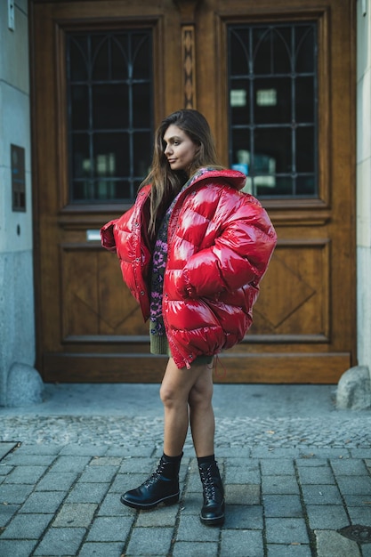 Zdjęcie pełna długość młodej kobiety w czerwonej kurtce stojącej na ulicy w mieście
