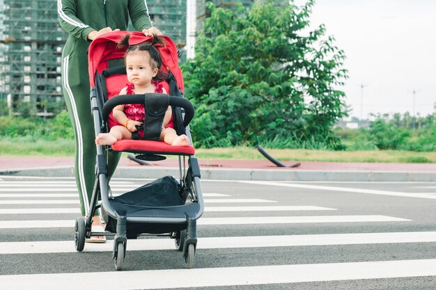 Pełna długość młodej matki popychającej wózek w parku Widok boczny młodej mamy idącej po parku