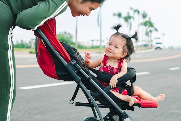 Pełna długość młodej matki popychającej wózek w parku Widok boczny młodej mamy idącej po parku