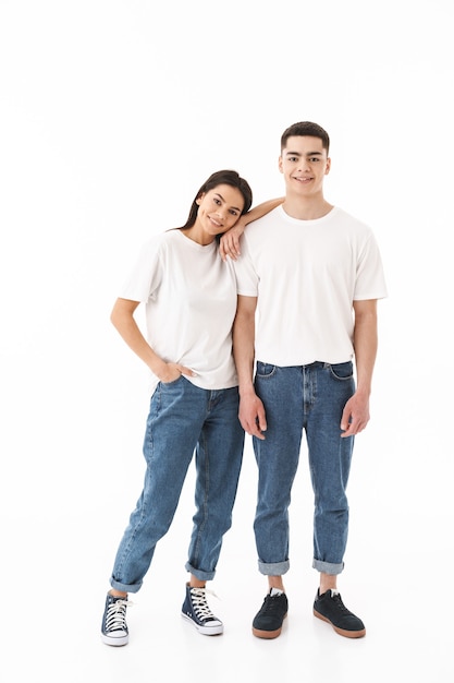 Pełna długość młodej pary w strojach casualowych, stojącej na białym tle nad białą ścianą, przytulającej się
