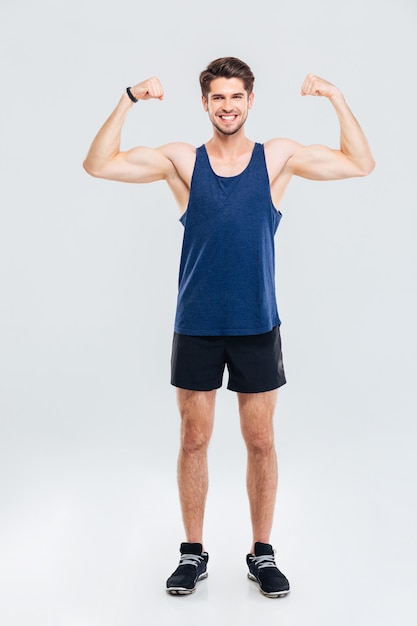 Pełna długość portret uśmiechniętego mężczyzny pokazującego jego bicepsy na szarym tle