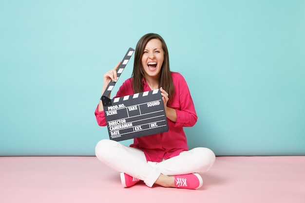Pełna długość strzału kobieta w różowej koszuli białych spodniach siedząca na podłodze z klapką do robienia filmów