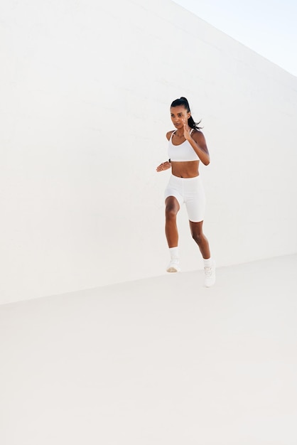 Pełna długość szczupłej kobiety biegnącej sprintem przed białą ścianą Młody lekkoatleta jogging outdoorsx9