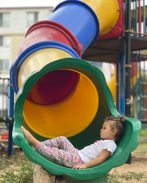 Zdjęcie pełna długość uroczej dziewczyny siedzącej na zjeżdżalni na placu zabaw