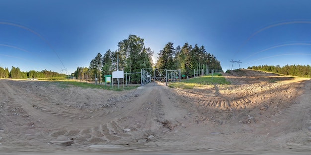 Pełna płynna panorama hdri 360 na szutrowej drodze przed ogrodzeniem granicy strefy zabronionej lub rezerwatu w lesie sosnowym w równokątnym rzucie sferycznym w pobliżu linii energetycznych i słupów wysokiego napięcia