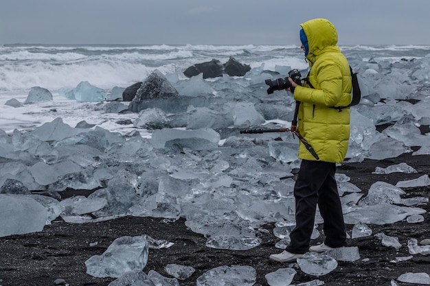 Zdjęcie pełna ramka fotografa na czarnej piaszczystej plaży z unikalnymi naturalnymi rzeźbami lodowymi z lodu lodowcowego