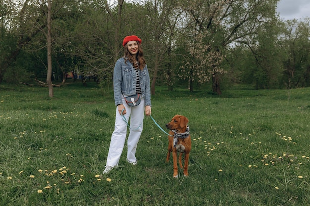 Pełna zawartość kobiety stojącej z szczeniakiem Rhodesian Ridgeback na smyczy na trawniku w parku