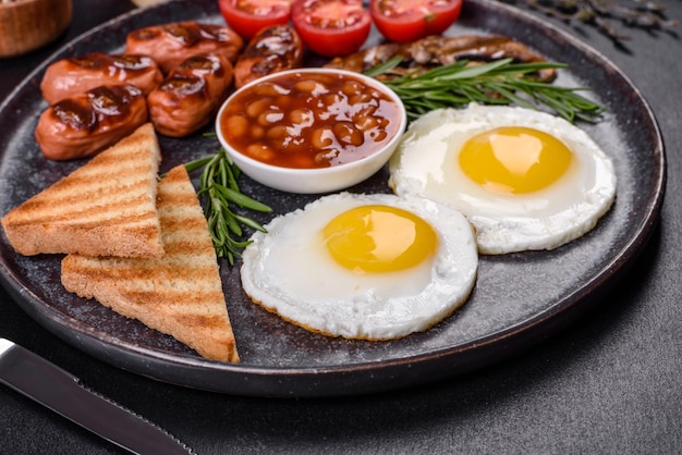Pełne angielskie śniadanie fasolowe jajka sadzone pieczone kiełbaski pomidory grzyby na ciemnym betonowym stole z opiekanym chlebem