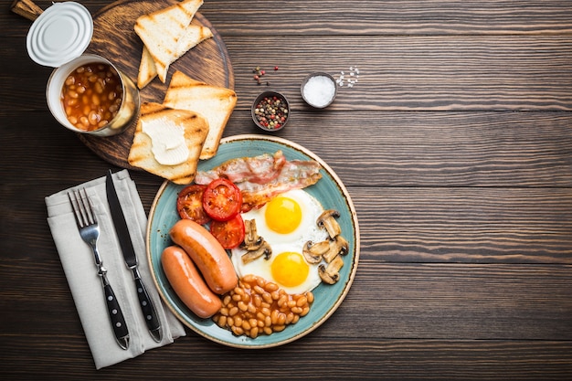 Zdjęcie pełne śniadanie angielskie z jajkiem sadzonym, kiełbasą, boczkiem, fasolą, pieczarkami, pomidorami
