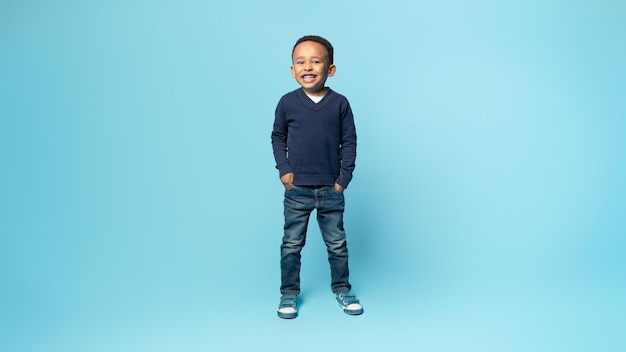 Pełne ujęcie Afroamerykanina, małego chłopca pozującego trzymającego się za ręce w kieszeniach, stojącego na niebiesko