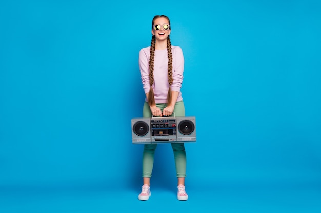 Pełne zdjęcie pozytywnego wesołego młodzieńca z warkoczami dziewczyna trzyma kasetę magnetofonową boombox chce imprezę retro na odpoczynek relaks w różowym swetrze trampki odizolowane na niebieskim tle