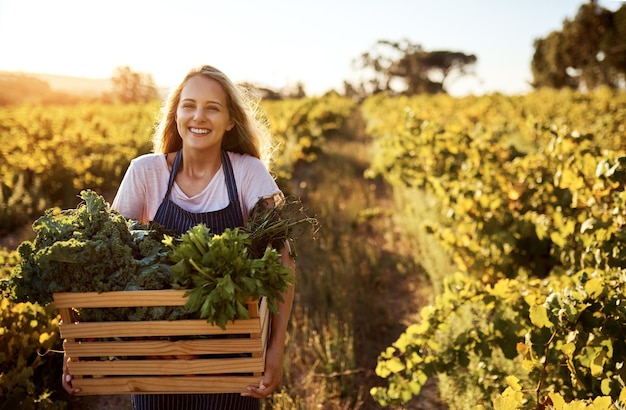 Pełne zielonej dobroci Przycięty portret atrakcyjnej młodej kobiety trzymającej skrzynię pełną świeżo zebranych produktów na farmie