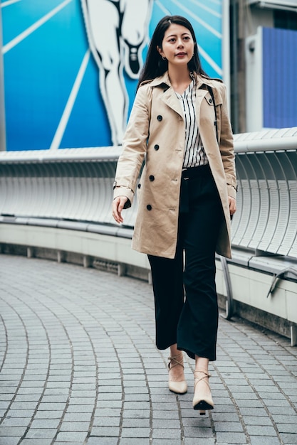 pełnej długości Asian kobieta idzie szybko na moście idzie do pracy rano w Osace w Japonii. elegancki pracownik biurowy businesswoman w dzielnicy biznesowej w centrum miasta, noszący wysokie obcasy, pewny siebie uśmiechnięty