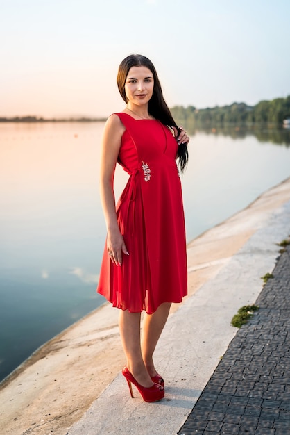 Pełnej długości kobieta w długiej sukni stojącej na plaży o zachodzie słońca