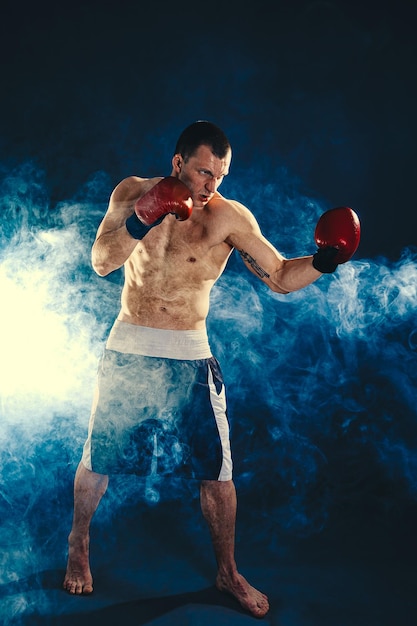 Pełnej długości muskularny kickbox lub zawodnik muay thai, który uderza na tle dymu Koncepcja sportu