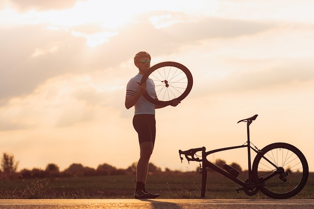 Pełnej długości portret przystojny brodaty mężczyzna w sportowym stroju, kasku i okularach, regulacja koła na czarnym rowerze na zewnątrz